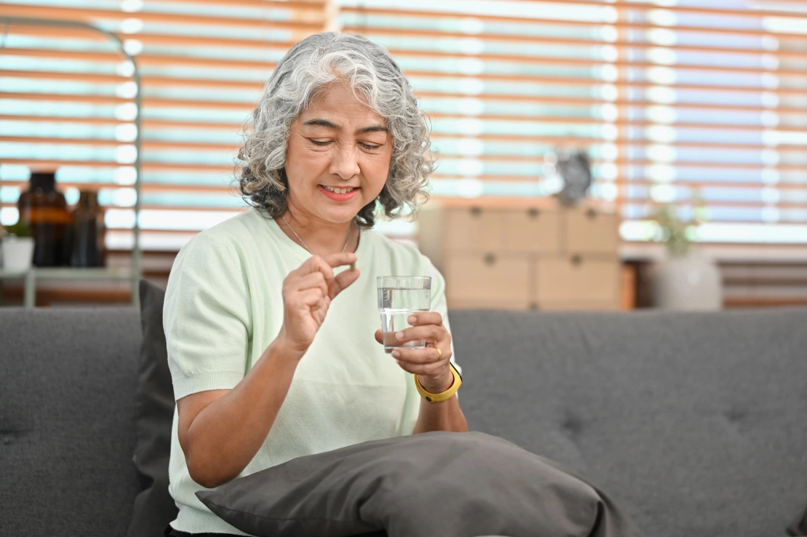 Smiling mature woman holding a supplement pill and glass of water at home, representing the question do menopause supplements work for hot flashes, mood swings, and overall well-being