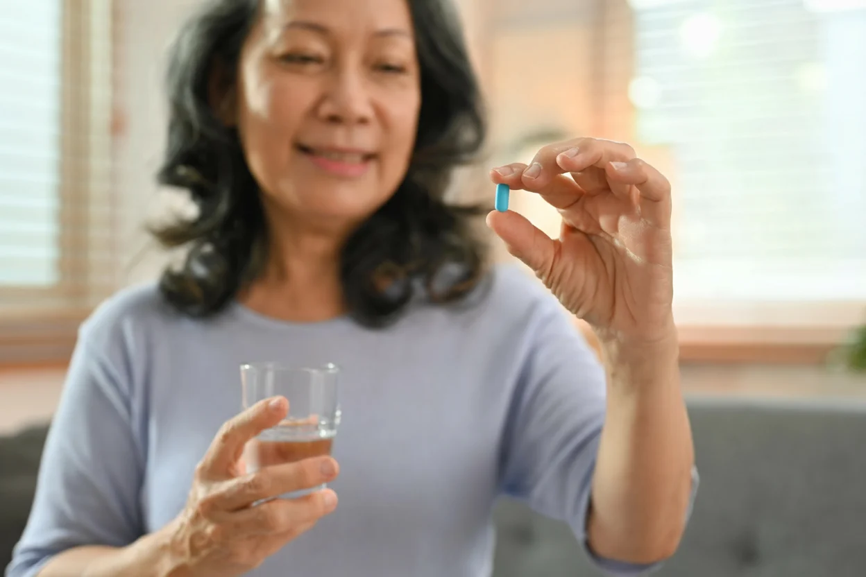 Smiling middle-aged woman holding Miror Thrive supplement tablet and a glass of water for post-menopause wellness