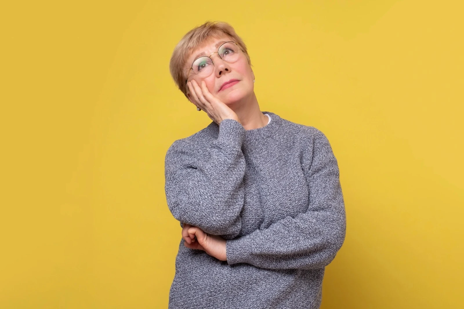 Senior woman in glasses looking thoughtful against yellow background, representing menopause mood swings and midlife wellness